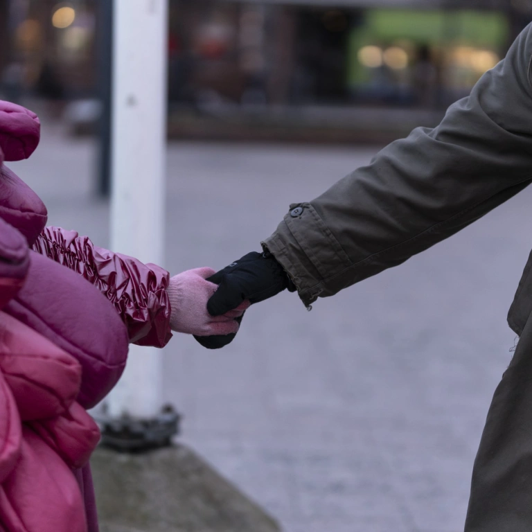 Kaksi ihmistä pitää toisiaan kädestä. Toisella on yllään tavallinen ulkotakki, toinen on pukeutunut pinkkiin suomukkaaseen esiintymisasuun.